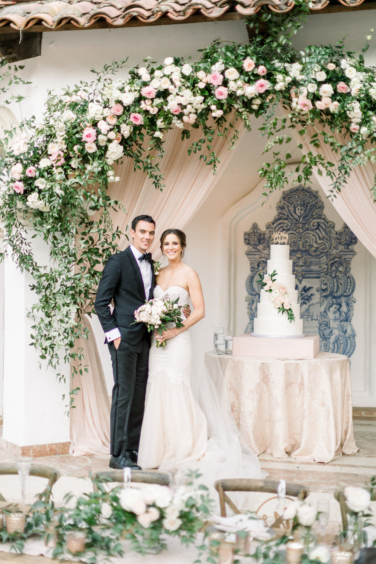 Beside the cake beneath a garland of garden roses and blush drapery