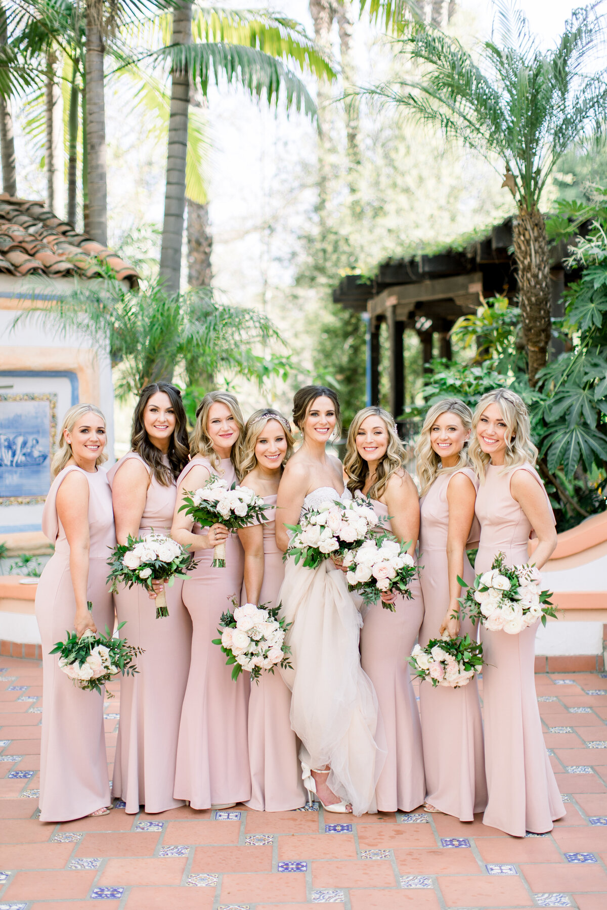 Bride and bridesmaids in blush gowns in a palm-shaded Spanish courtyard