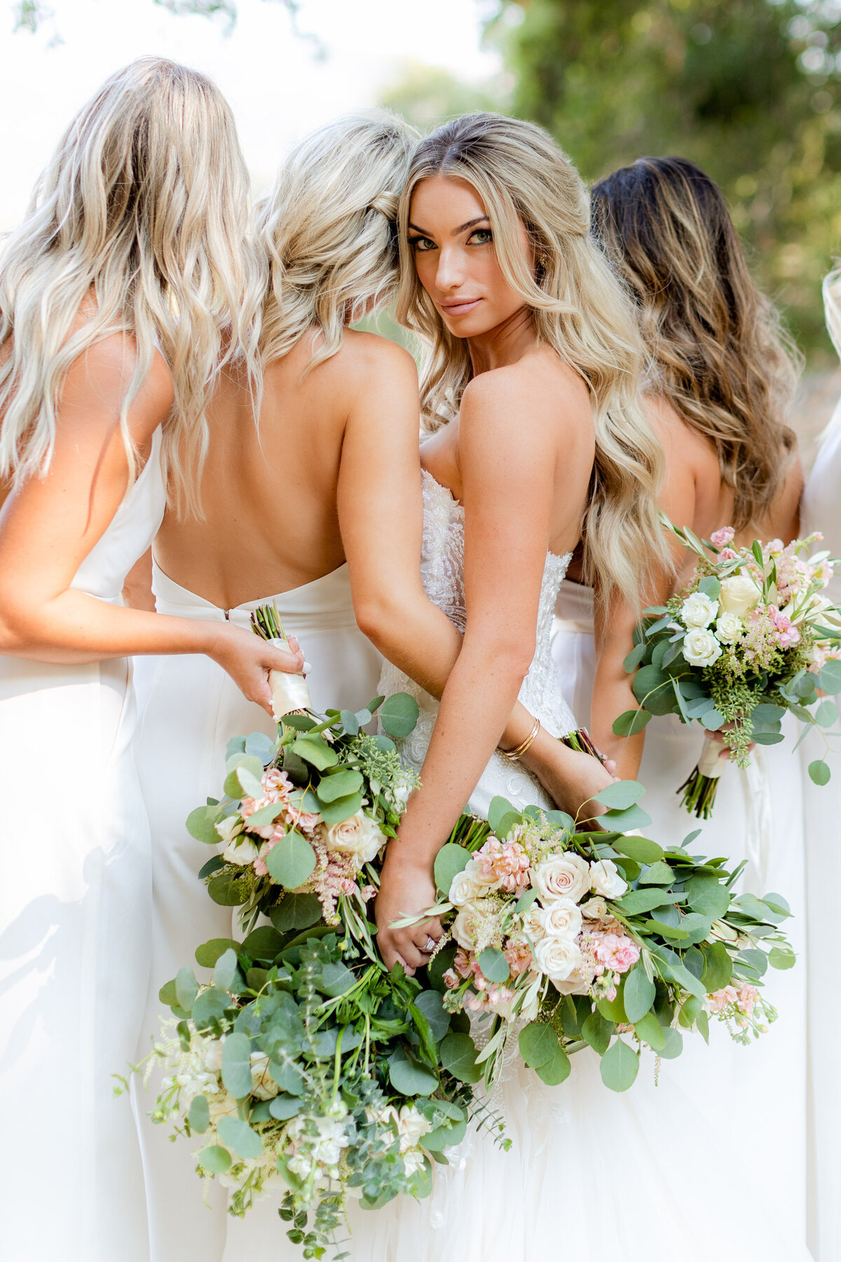The bride glances back, eucalyptus and blush roses gathered around her