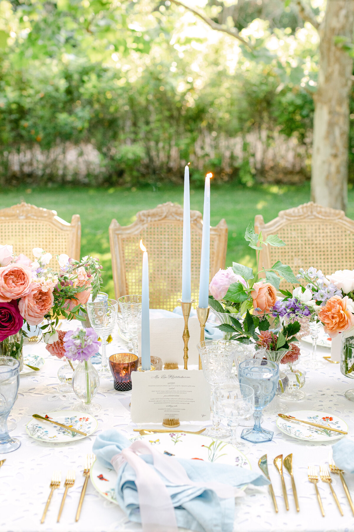 Blue tapers and coral garden roses down a table set with butterfly china