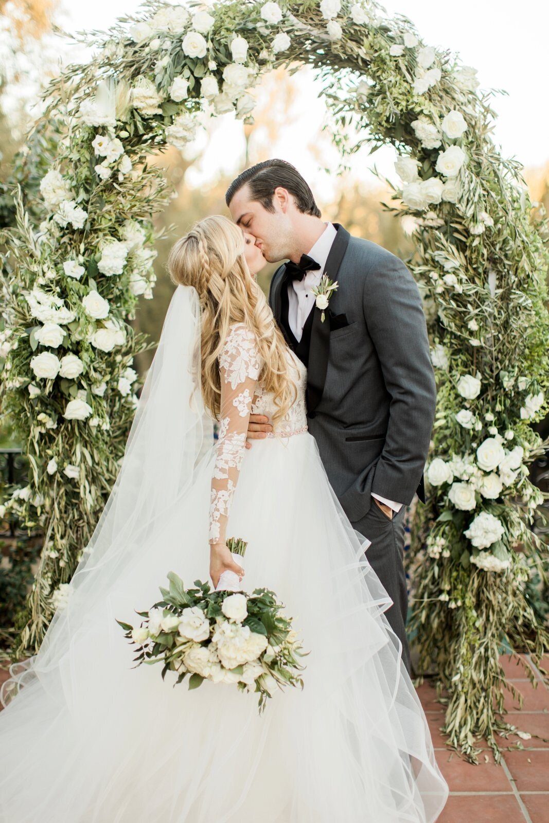 A kiss beneath a full circle of olive branches and white roses