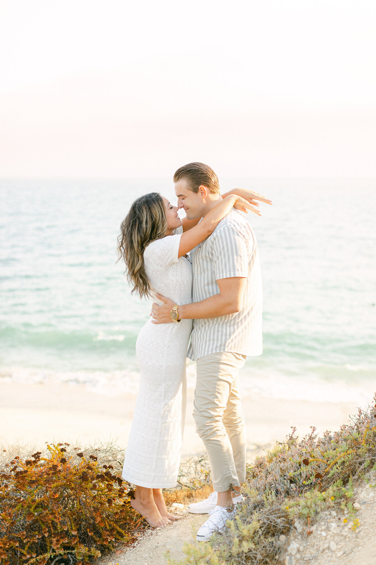 Barefoot couple embracing on a coastal bluff at sunset