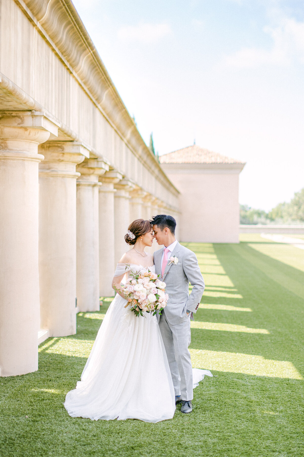 Foreheads together along the colonnade, shadows striping the lawn