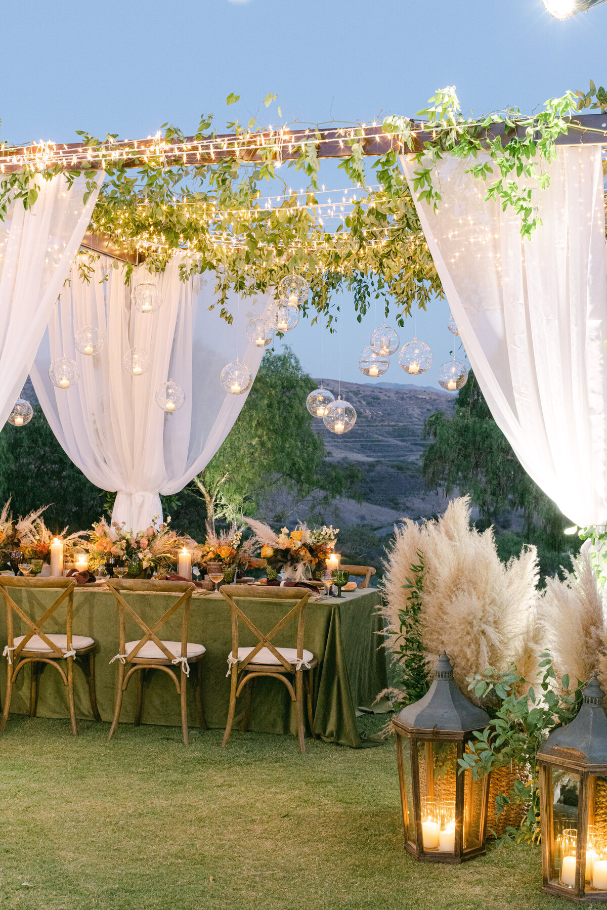 Candlelight in glass orbs over a green velvet table as the sky goes blue