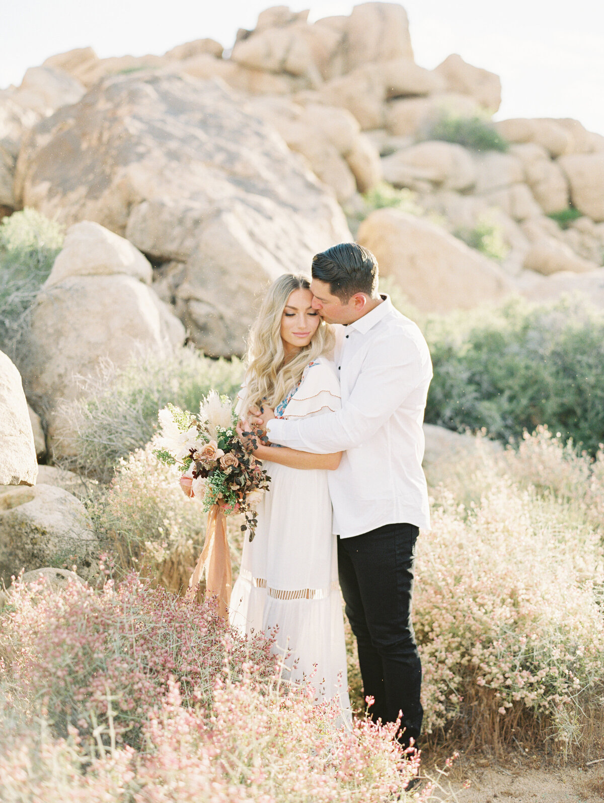 A kiss at her temple among the desert boulders, wild buckwheat at their feet
