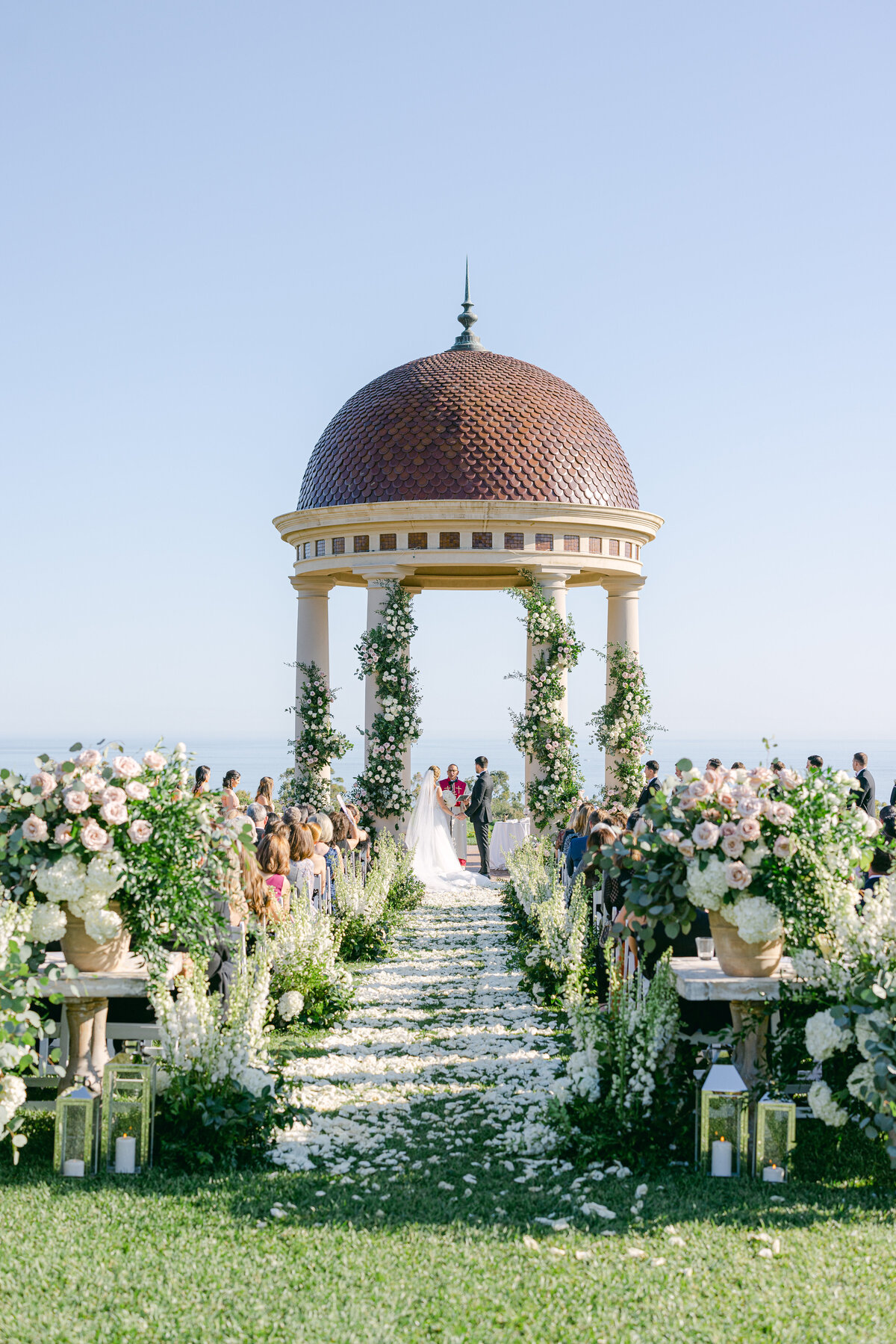 Ceremony beneath the rotunda above the Pacific at Pelican Hill, a petal aisle lined with blush urns