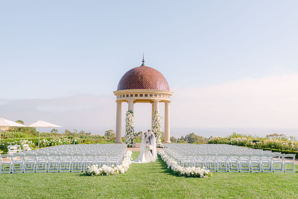 Ceremony set at the Pelican Hill rotunda above the Pacific, an aisle lined with white flowers