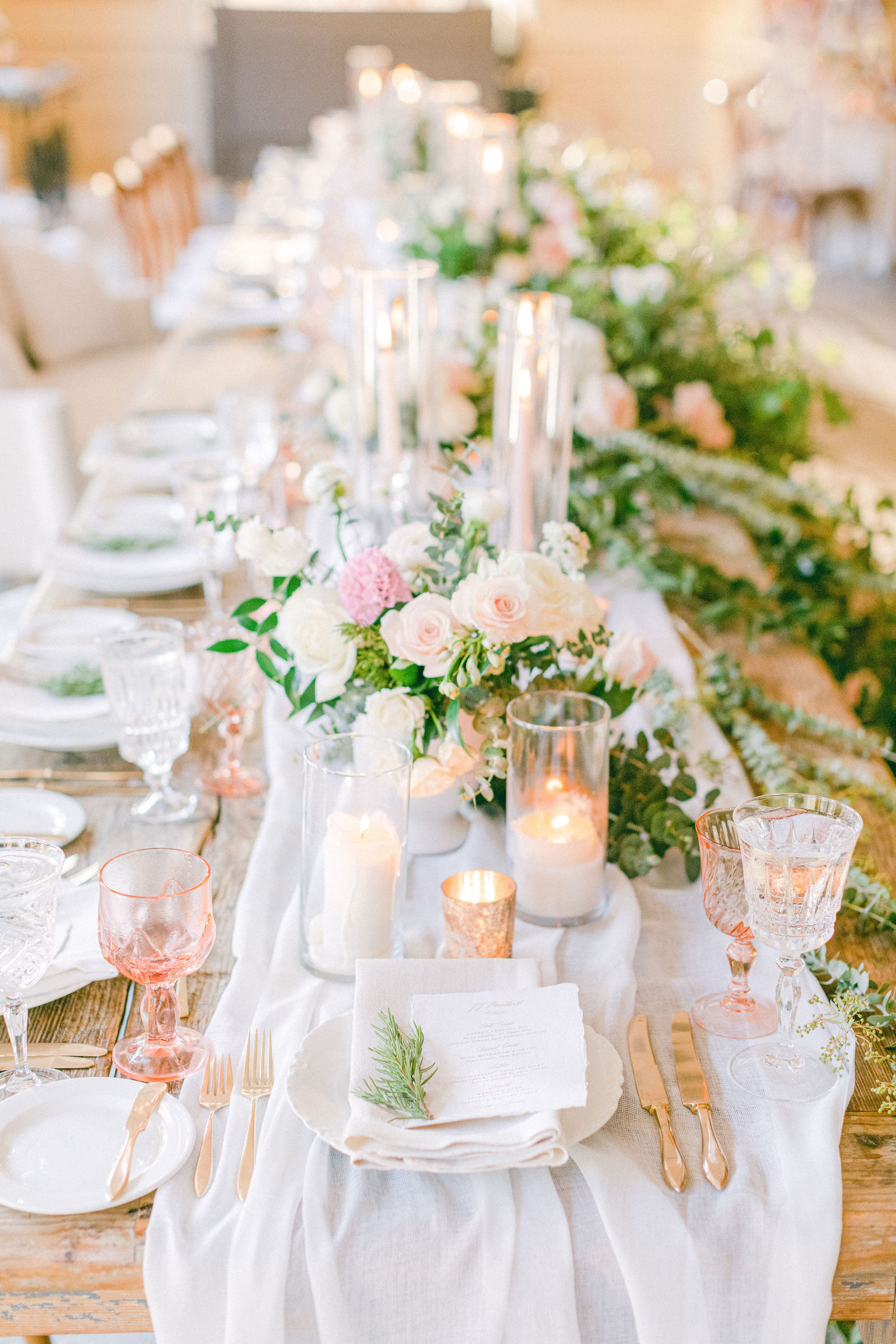 The tables set with gold flatware, greenery and candlelight