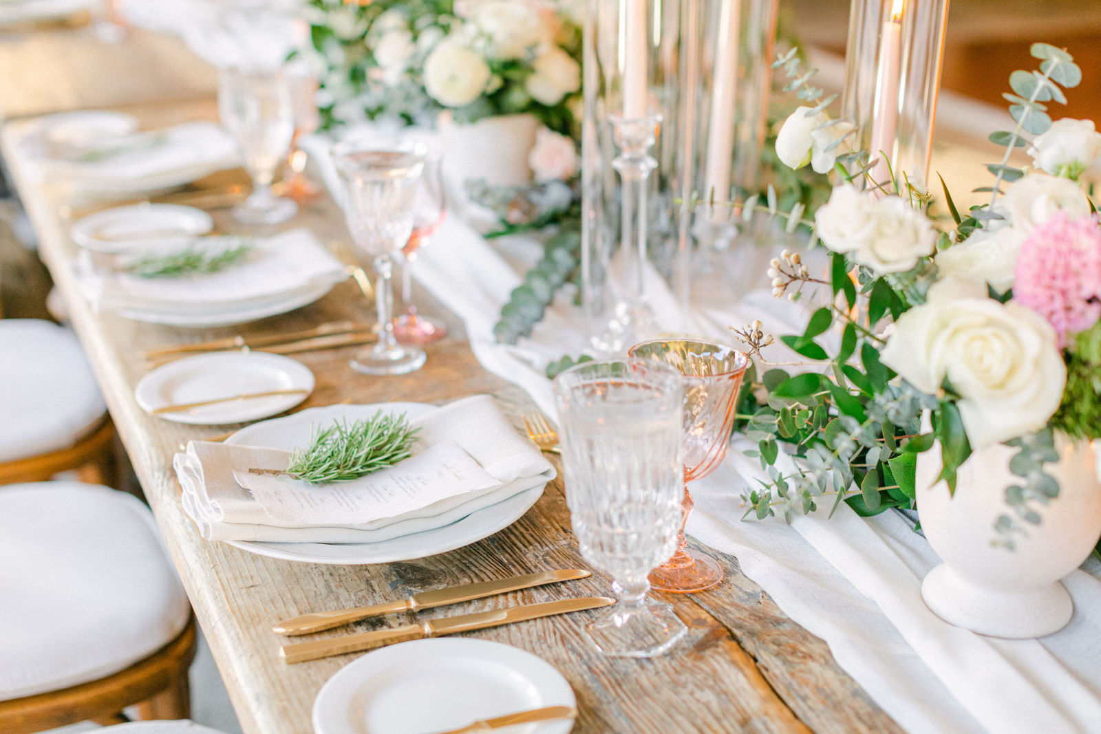 The tables set with gold flatware, greenery and candlelight