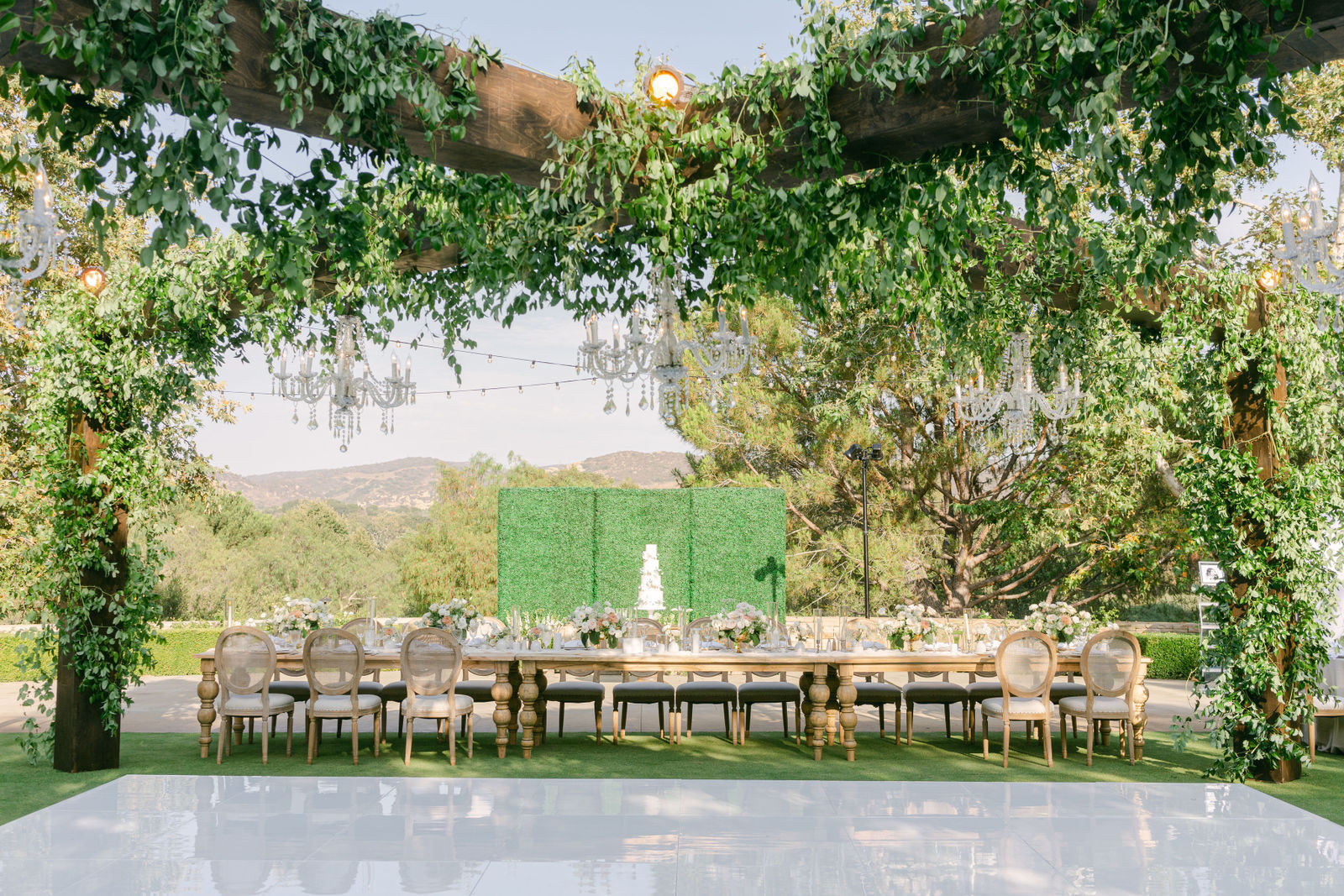 A reception beneath a pergola of vines at Shady Canyon, chandeliers overhead and the dance floor laid