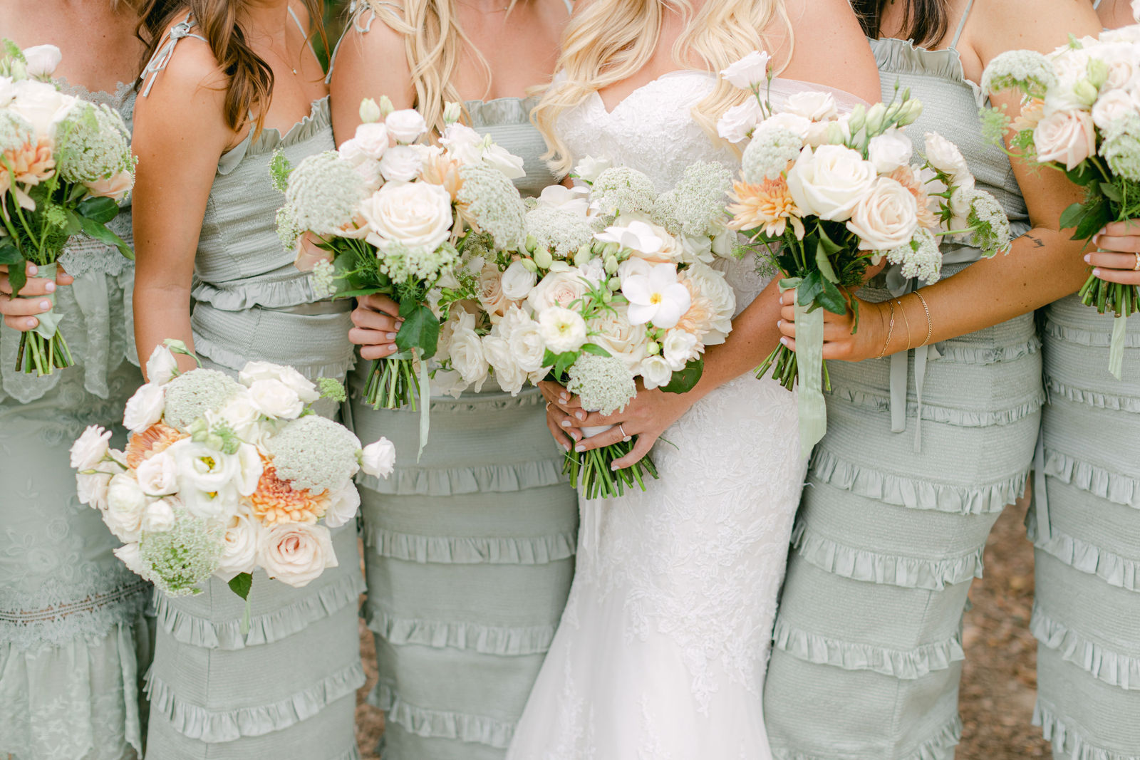 Bridesmaids in sage green with bouquets of white roses, dahlias and ranunculus