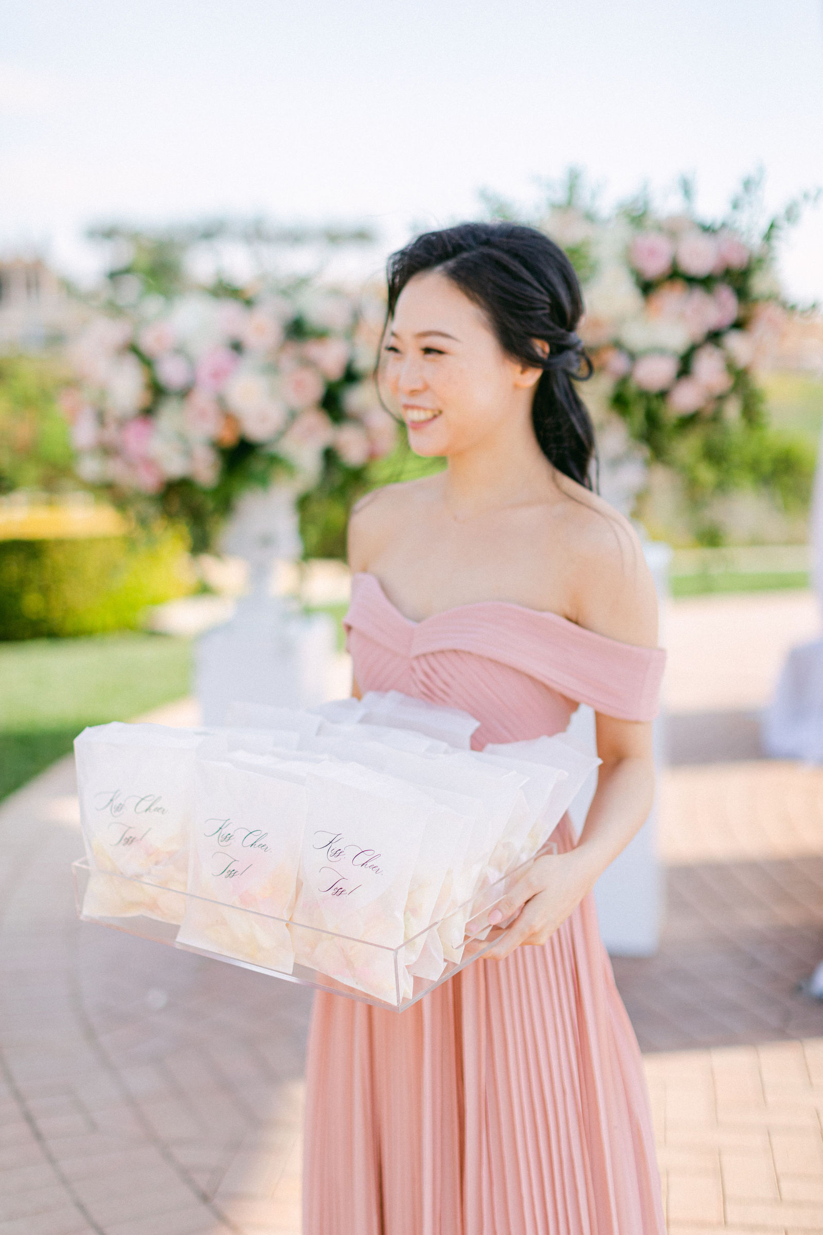 A bridesmaid in blush carrying the welcome gifts across the terrace at Pelican Hill