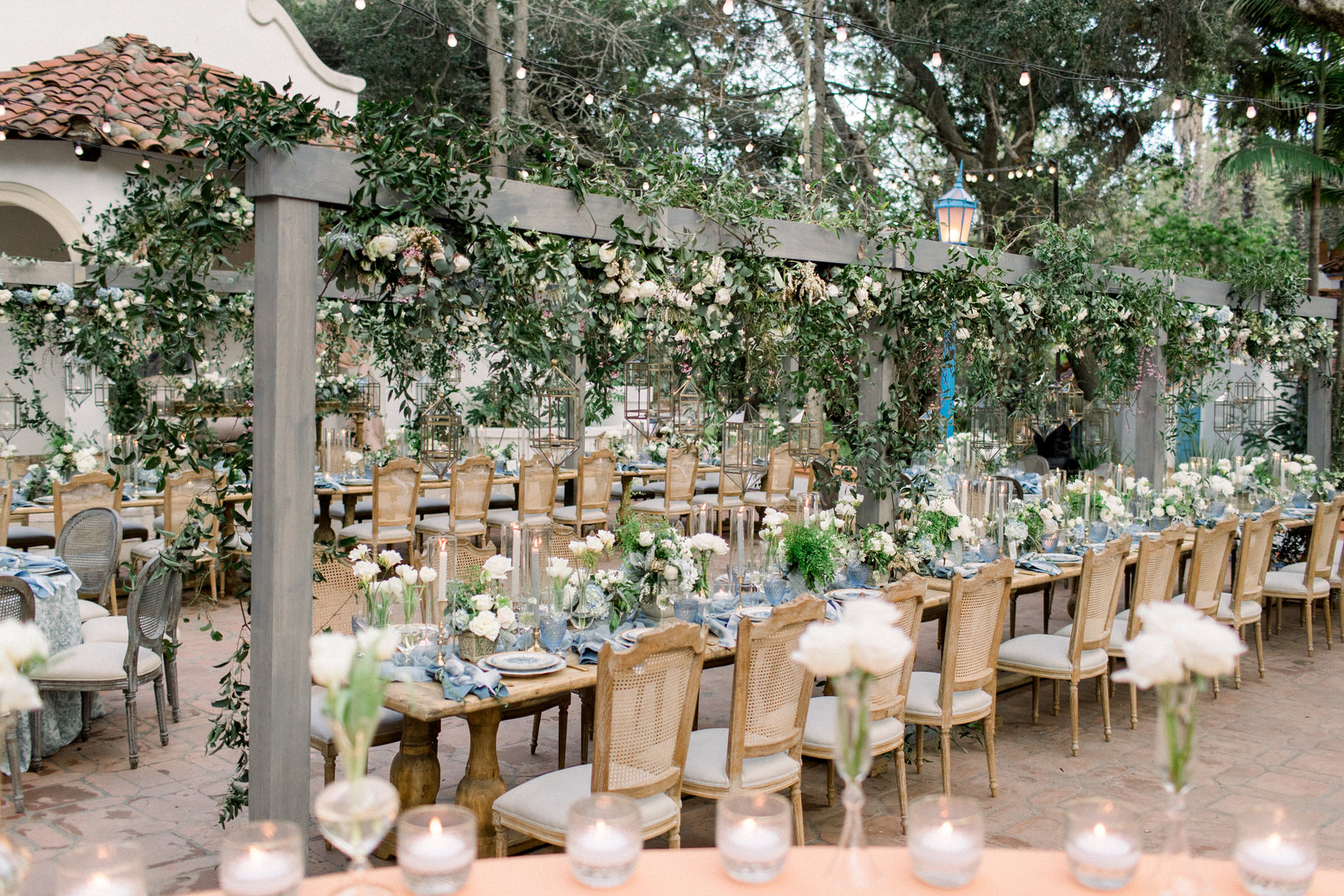 Long reception tables under the oaks at Rancho Las Lomas, greenery and lanterns overhead