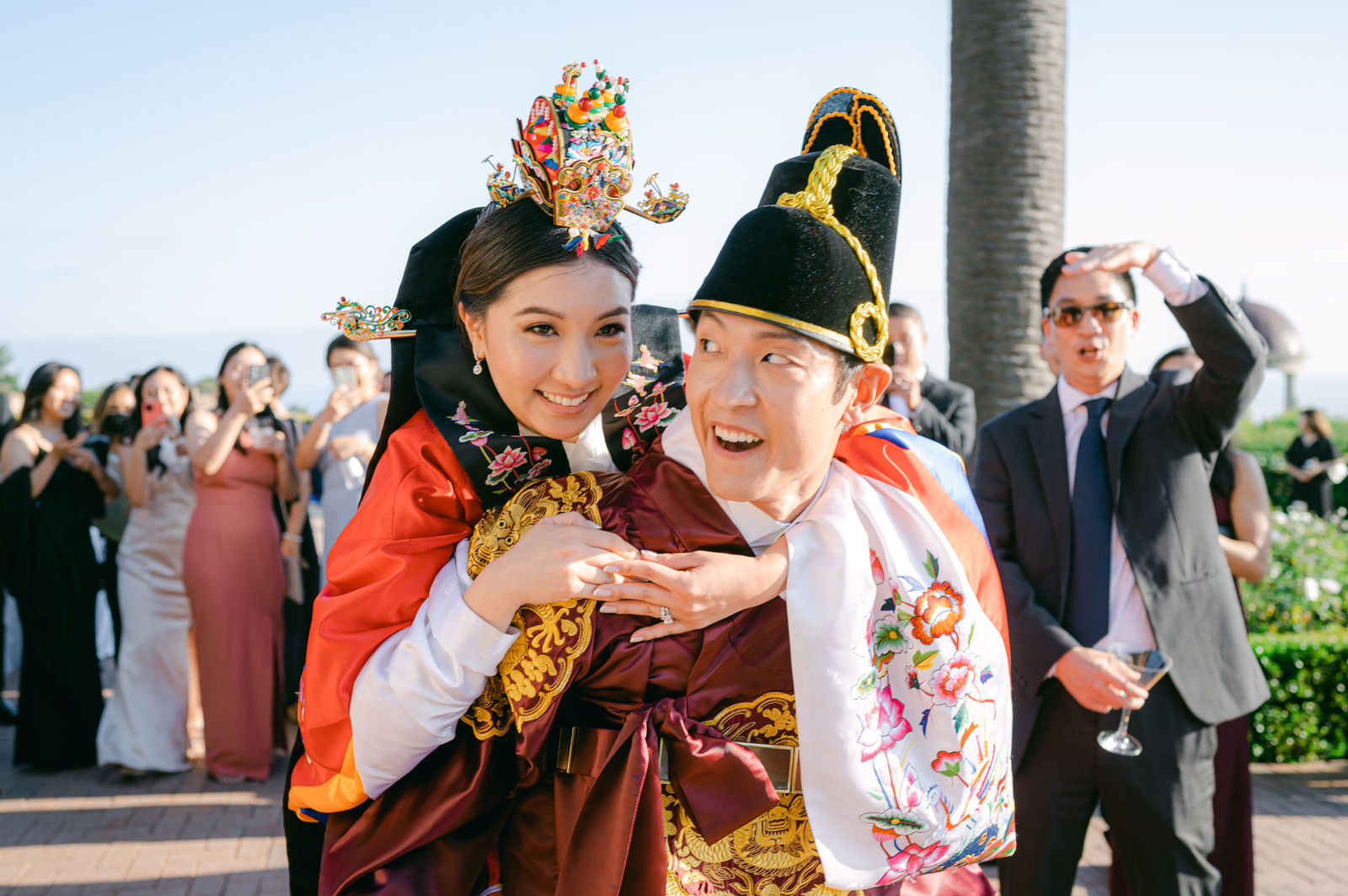 The groom carrying the bride on his back during the paebaek at Pelican Hill, both in hanbok